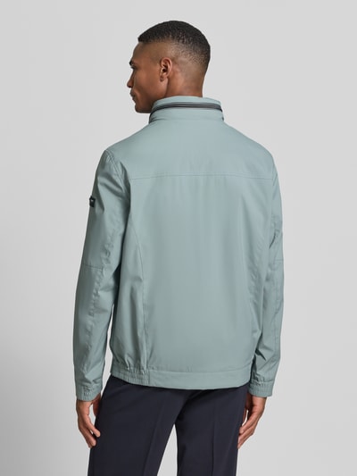 Männermodel trägt Regular Fit Jacke mit Stehkragen von bugatti, hellblau, glatte Textur, Logo-Detail, Rückansicht Ganzkörperansicht. Kontext: Herren Jacke von bugatti, Stehkragen, Regular Fit, Logo-Detail, verstaubare Kapuze, Zweiwege-Reißverschluss, Eingrifftaschen, elastische Ärmelabschlüsse, Rückenlänge bei Größe 50: 68 cm, Schulterbreite bei Größe 50: 42 cm, Brustweite bei Größe 50: 50 cm, Ärmellänge bei Größe 50: 65 cm.