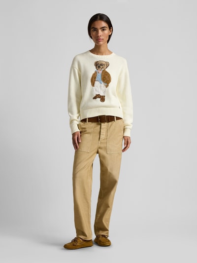 Kobiece modelka nosi Regular Fit Strickpullover mit Polo Bear von Polo Ralph Lauren, efekt: jednolity kolor, krój regular fit, aplikacja: polo bear, kształt kołnierza: okrągły dekolt, rękawy: długi rękaw, zakończenie rękawów: prążkowane, wykończenie: prążkowane, wykończenie materiału: dzianina, materiał: bawełna. Ganzkörperansicht von vorne.