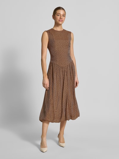 Vrouwenmodel draagt Bubble jurk met ronde hals model 'KRISSI' van YAS, lyocellmix, getailleerde fit, midi, bruine stof met stippen, vooraanzicht hele lichaam.