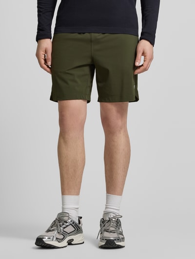 Männermodel trägt Regular Fit Shorts mit Logo-Print von Fabletics in Olivgrün, elastischer Bund, Eingrifftaschen, Ganzkörperansicht von vorne.
