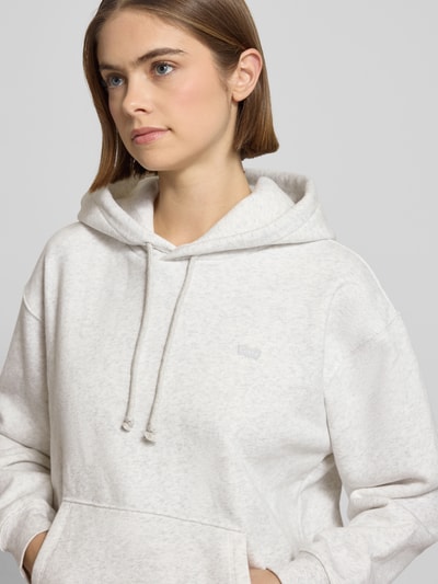Frauenmodel trägt Hoodie mit Kapuze von Levi's®, Baumwoll-Mix in Hellgrau, lockerer Schnitt, Label-Detail, Nahaufnahme Oberkörper.