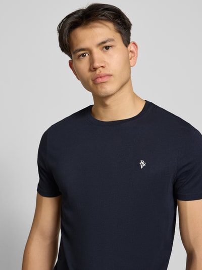 Männermodel trägt Basic Slim Fit T-Shirt mit Flock-Logo auf der Brust von REVIEW, dunkelblauer Baumwoll-Viskose-Mix, Nahaufnahme Oberkörper.