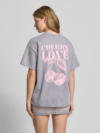 Modelka nosi damski t-shirt Oversized T-Shirt aus Bio-Baumwolle Modell 'KINNA LIFE' od Only, z efektem melanżu, nadruk z napisem, okrągły dekolt, krótki rękaw, zakończenia i dół z zrolowanym brzegiem, 100% bawełna ekologiczna, widok całej sylwetki od tyłu.