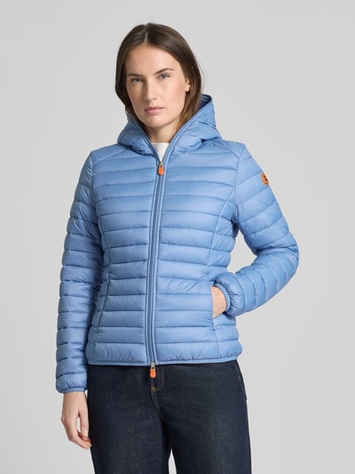 Frauenmodel trägt hellblaue Slim Fit Steppjacke im Zweiwegereißverschluss Modell 'Daisy' von SAVE THE DUCK, Kapuze, Eingrifftaschen, Ganzkörperansicht von vorne.