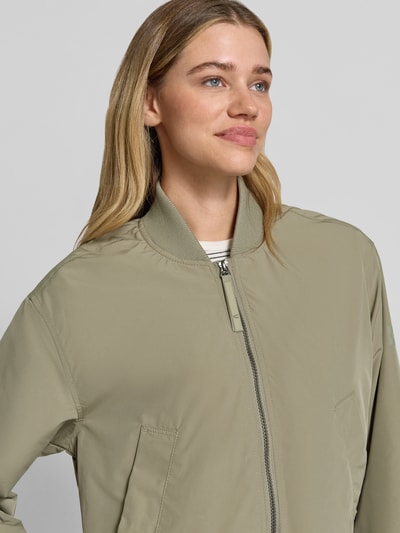 Frauenmodel trägt Regular Fit Jacke mit Stehkragen von camel active in Olivgrün, Zweiwege-Reißverschluss, Eingrifftaschen, Nahaufnahme Oberkörper.