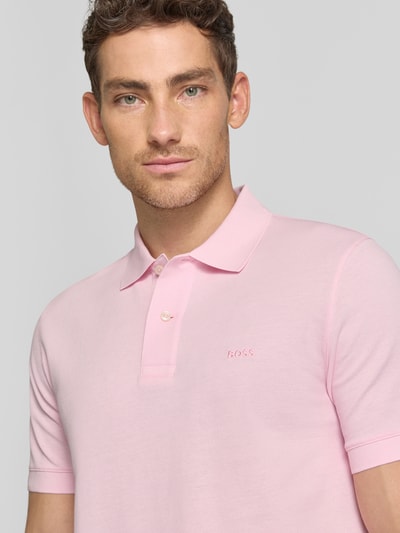 Männermodel trägt Regular Fit Poloshirt aus reiner Baumwolle Modell 'PALLAS' von BOSS in Rosa, Piqué-Struktur, Label Stitching, Nahaufnahme Oberkörper.