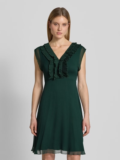 Modelka nosi Knielanges Kleid mit Rüschen und V-Ausschnitt von Zero, szyfon, taliowany krój, długość do kolan, dekolt w serek, falbany, rękawy z falistym wykończeniem, zamek błyskawiczny z tyłu, długość tyłu w rozmiarze 36: 84 cm, szerokość w rozmiarze 36: 40 cm, ciemnozielony, gładka faktura, całkowity widok z przodu.