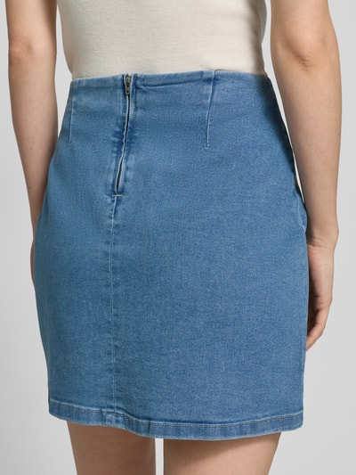 Frauenmodel trägt eng anliegenden Jeansrock aus Baumwoll-Mix Modell 'NELLY' von Vero Moda in Denim-Optik, Mini-Länge, Ganzkörperansicht Rückansicht.