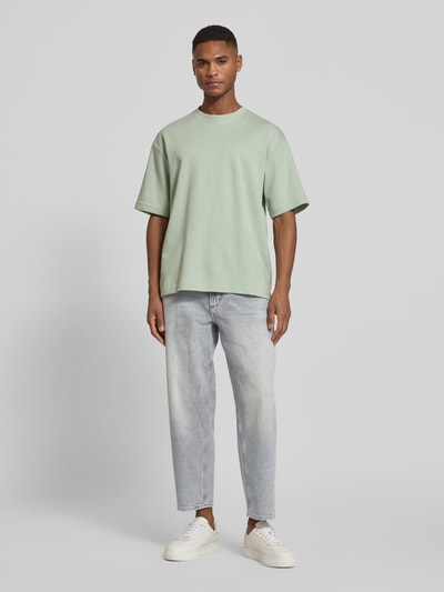 Männermodel trägt Tapered Fit Jeans aus Baumwoll-Mix Modell 'ARLO' von BOSS Orange, unifarbenes Denim, 5-Pocket-Design, Ganzkörperansicht von vorne.