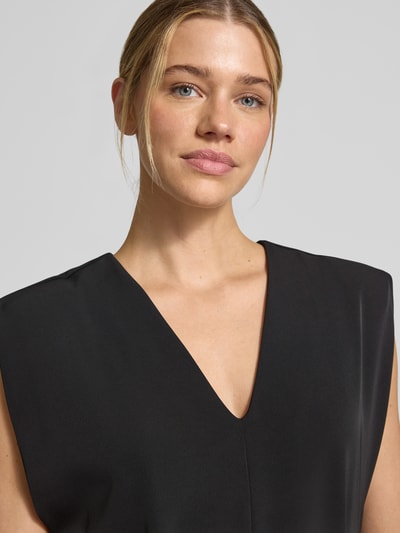 Frauenmodel trägt Jumpsuit mit V-Ausschnitt und Bindegürtel von Comma, schwarzer Material-Mix mit Stretch-Anteil, Nahaufnahme Oberkörper.