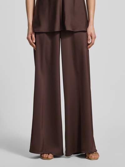 Kobiece modelka nosi Stoffhose mit elastischem Bund od V by Vera Mont w kolorze czekoladowobrązowym, z satynową teksturą, krój relaxed fit, szerokie nogawki, szerokość w rozmiarze 36: 28 cm, długość wewnętrzna nogawki w rozmiarze 36: 79 cm, całkowity widok z przodu.