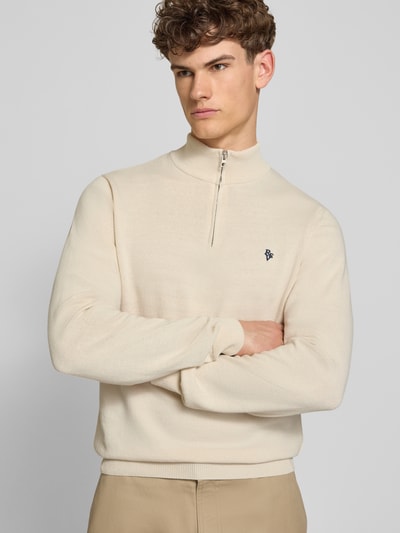 Męski model nosi Troyer mit Logo-Stitching und kurzem Reißverschluss od REVIEW z mieszanki bawełny, krój nowoczesny, kołnierz zapinany, krótki zamek błyskawiczny, wyhaftowane logo, prążkowane wykończenia, długość tyłu w rozmiarze M 65 cm, długość rękawów 66 cm, jasny beż, prosta faktura, gładkie powierzchnie, całkowity widok z przodu.