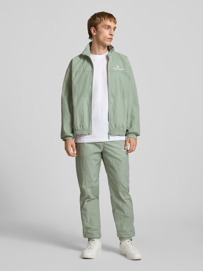 Männermodel trägt Straight Fit Stoffhose mit Logo-Stitching Modell 'Nayla' von SERGIO TACCHINI in hellem Grün, Ganzkörperansicht von vorne, Herren, elastischer Bund mit Tunnelzug, elastische Beinabschlüsse, Innenbeinlänge bei Größe M 77 cm, Anzug-Stoff