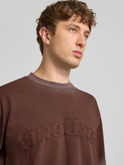 Męski model nosi T-Shirt mit Label-Stitching und Rundhalsausschnitt von ANOTHER COTTON LAB, brązowy, bawełna, krój relaxed fit, długość tyłu 67 cm, zbliżenie na górną część ciała