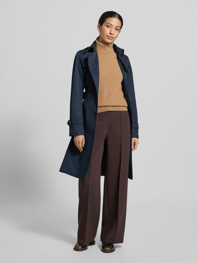 Modelka nosi Trencz mit Stoffgürtel od Jake*s Casual, mieszanka bawełny, taliowany krój, pasek z materiału, wykładany kołnierz, wpuszczane kieszenie, listwa guzikowa, długość tyłu w rozmiarze 36: 99 cm, szerokość ramion: 40 cm, szerokość w klatce piersiowej: 41 cm, długość rękawów: 64 cm, ciemnoniebieski kolor, gładka tekstura, widok całej sylwetki z przodu.