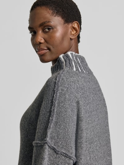 Kobiece modelka nosi sweter z dzianiny 'Strickpullover mit Stehkragen und überschnittenen Schultern' od Apricot, krój relaxed fit, Dwa kolory, stójka, Długość tyłu w rozmiarze S: 79 cm, Długość rękawów w rozmiarze S: 49 cm, szaro-biała faktura, widoczne przeszycia, detaliczna faktura tkaniny, zbliżenie górnej części ciała.