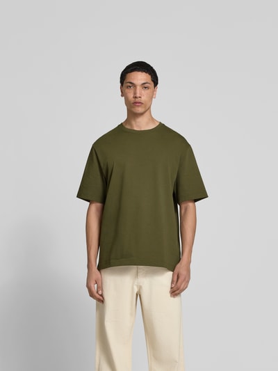 Männermodel trägt T-Shirt mit Rundhalsausschnitt von Filippa K in Olivgrün, Baumwolle, Relaxed Fit, Kurzarm, Ganzkörperansicht von vorne.