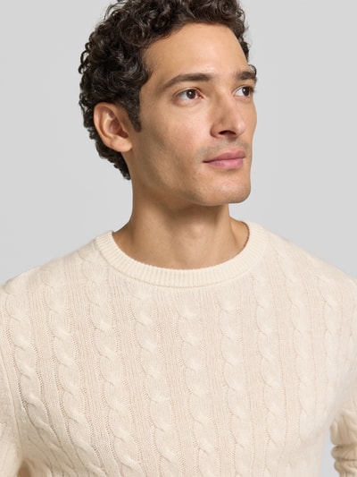 Männermodel trägt Slim Fit Strickpullover aus reinem Kaschmir mit Zopfmuster von Christian Berg Men in Creme, Nahaufnahme Oberkörper. Reines Kaschmir, Rundhalsausschnitt, langärmeliges Design, gerippte Abschlüsse.