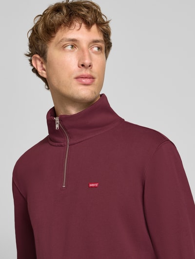 Männermodel trägt Regular Fit Pullover aus reiner Baumwolle von Levi's® in Dunkelrot mit dezentem Logo, Nahaufnahme Oberkörper.