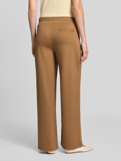 Frauenmodel trägt Wide Fit Hose mit Viskose-Anteil Modell 'Kate' von ICHI in Braun, teilelastischer Bund, Bundfalten, Ganzkörperansicht Rückansicht.
