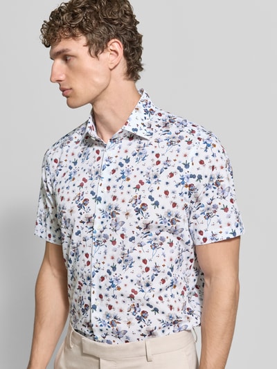 Männermodel trägt Regular Fit Business-Hemd aus Baumwolle mit Kentkragen von Christian Berg Men, Allover-Look, Nahaufnahme Oberkörper. Rückenlänge 78 cm, Schulterbreite 47 cm, Ärmellänge 23 cm, reine Baumwolle, Floralmuster in Weiß, Blau und Rot.