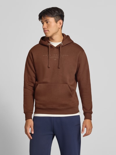 Männermodel trägt Relaxed Fit Hoodie aus Baumwoll-Mix mit Label-Detail von Alpha Industries, braun, Känguru-Tasche, Ganzkörperansicht von vorne.