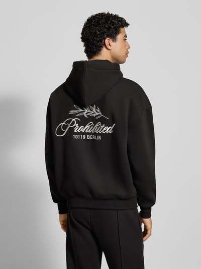 Männermodel trägt Oversized Hoodie mit Label-Stitching von PROHIBITED aus schwarzem Baumwoll-Mix mit Kapuze, Känguru-Tasche und gerippten Abschlüssen, Rückenlänge bei Größe M 67 cm, Ärmellänge 59 cm, Rückenansicht Ganzkörperansicht.