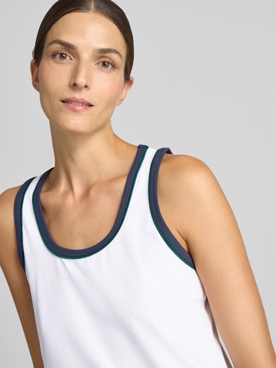 Frauenmodel trägt Top mit Rundhalsausschnitt Modell 'Tegan' von VARLEY, weiß mit blauen Rändern, tailliert, Nahaufnahme Oberkörper. Elastischer Material-Mix, Rückenlänge bei Größe S 62 cm.
