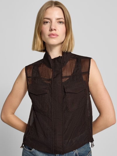 Frauenmodel trägt Weste in semitransparentem Design von monari, tailliert, Stehkragen, Brusttaschen, schwarze Farbe, Nahaufnahme Oberkörper.