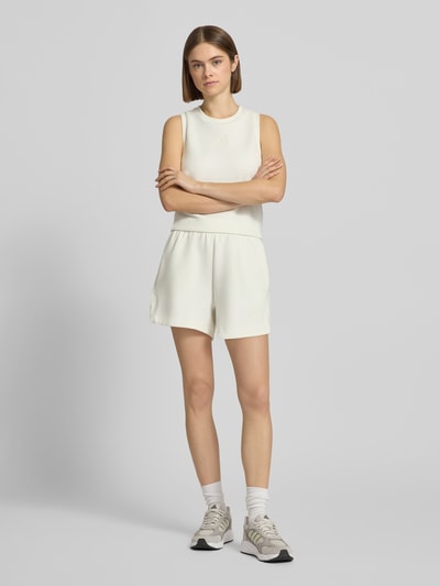 Frauenmodel trägt Shorts mit Label-Print von adidas Sportswear in Creme, lockerer Schnitt, elastischer Bund, Material-Mix, Ganzkörperansicht von vorne.