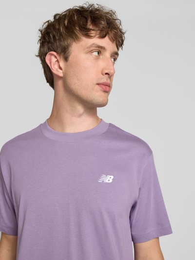 Männermodel trägt T-Shirt mit Logo und Rundhalsausschnitt von New Balance in Flieder, Reine Baumwolle, Regular-Fit, Nahaufnahme Oberkörper. Rückenlänge bei Größe M: 74 cm.