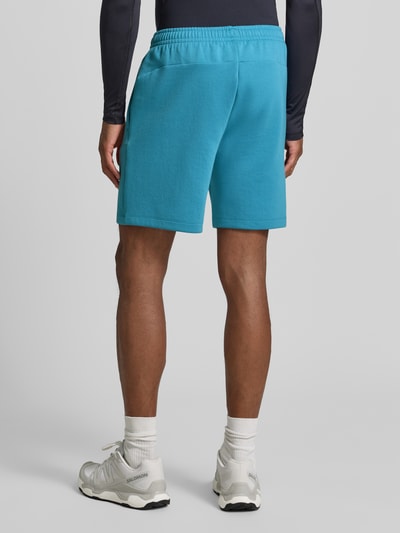 Mężczyznamodel nosi szorty z kieszenią zapinaną na zamek błyskawiczny od Under Armour, mieszanka bawełny, krój regular fit, logo, elastyczny pas, szerokość w rozmiarze M: 39 cm, długość wewnętrzna nogawki w rozmiarze M: 18 cm, jasnoniebieski, widok całej sylwetki z tyłu