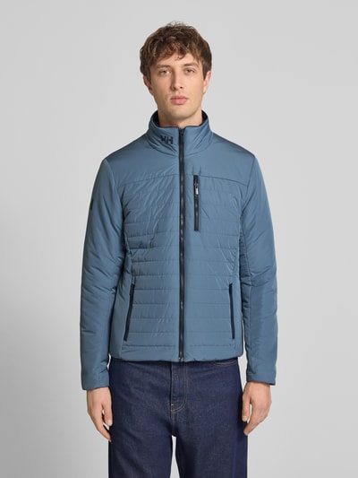 Männermodel trägt Regular Fit Jacke mit opstaande kraag van Helly Hansen in blauw met logoprint, steekzakken en ritssluiting, ganzkörperansicht van voren. Ruglengte maat M: 70 cm, schouderbreedte: 46 cm, borstwijdte: 54 cm, mouwlengte: 69 cm.
