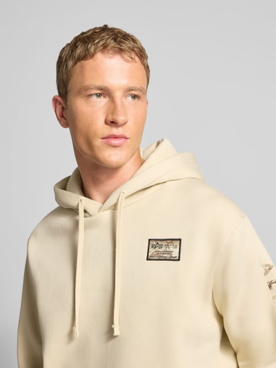 Męski model nosi Hoodie z label-stitching model 'Camo Sleeve' od Alpha Industries, kremowy bawełniany mix, ujęcie z przodu, zbliżenie na górę.