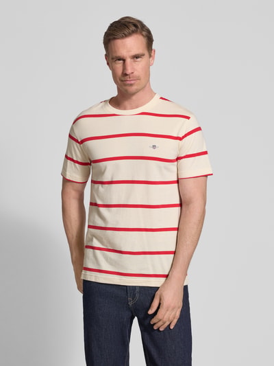Männermodel trägt Regular Fit T-Shirt mit Logo-Stitching von Gant, creme mit roten Streifen, reine Baumwolle, Rundhalsausschnitt, Ganzkörperansicht von vorne. Rückenlänge bei Größe M: 68 cm.
