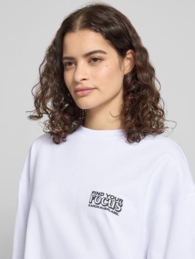 Frauenmodel trägt Oversized Longsleeve mit Statement-Print von Karo Kauer, reine Baumwolle, weiß, Rundhalsausschnitt, Nahaufnahme Oberkörper.