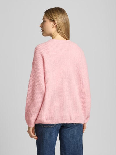 Frauenmodel trägt Cardigan mit V-Ausschnitt Modell 'EAST' von American Vintage, relaxed Fit, Strukturstrick in Rosa, Ganzkörperansicht Rückansicht.