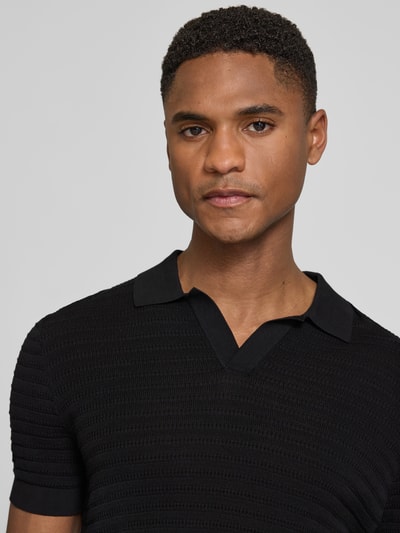 Männermodel trägt schwarzes Slim Fit Strick-Poloshirt mit Strukturmuster Modell 'BRAIAN' von Drykorn, reine Baumwolle, Nahaufnahme Oberkörper.