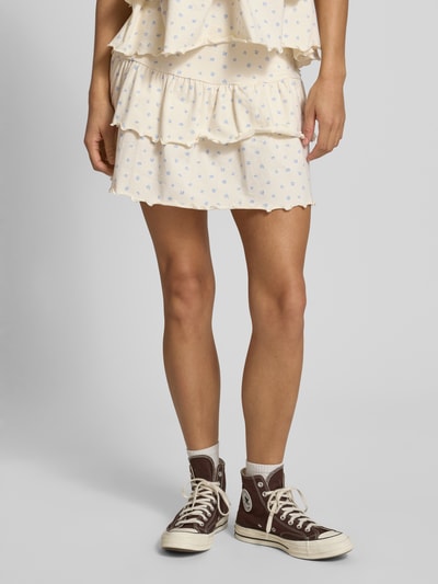 Frauenmodel trägt Minirock im Stufen-Look von REVIEW aus Baumwoll-Elasthan-Mix, A-Linie, Volants, creme mit blauen Details, Nahaufnahme Unterkörper.