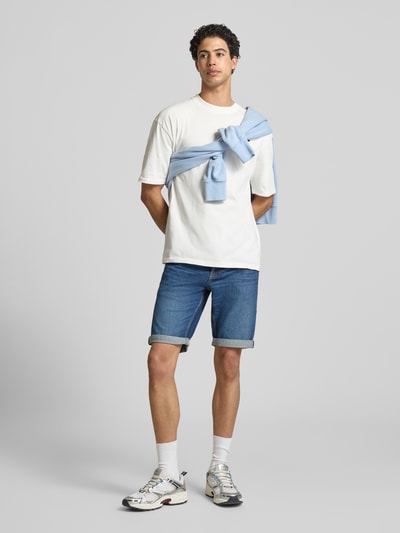Männermodel trägt Regular Fit Jeansshorts aus Baumwoll-Mix Modell 'RONNIE' von Tommy Jeans in Denim-Optik mit Kontrastnähten, Ganzkörperansicht von vorne.