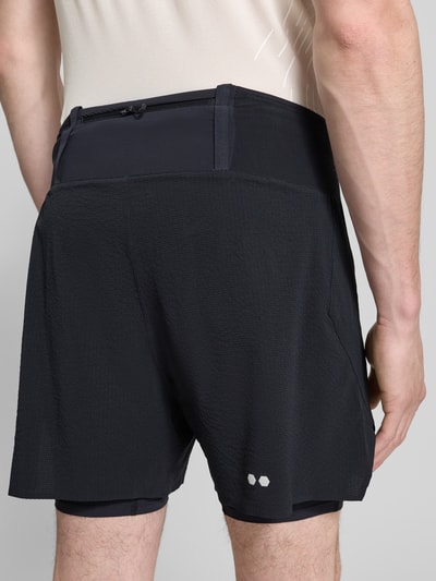 Männermodel trägt Shorts im 2-in-1-Look Modell 'SENSE AERO 2IN1' von Salomon in Schwarz, Material-Mix mit Stretch, Ganzkörperansicht Rückansicht.