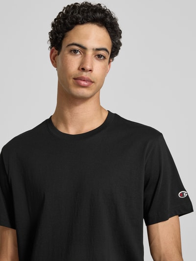 Männermodel trägt T-Shirt mit Rundhalsausschnitt im 2er-Pack von CHAMPION in Schwarz aus Reine Baumwolle, Regular-Fit, Label-Detail, Nahaufnahme Oberkörper.