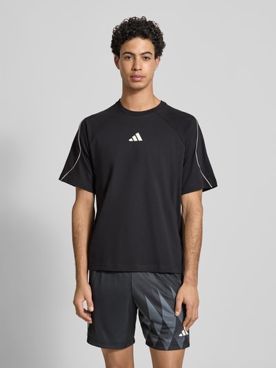 Männermodel trägt T-Shirt mit Label-Print von adidas Sportswear, schwarze Baumwolle, Regular-Fit, gerippter Rundhalsausschnitt, Ganzkörperansicht von vorne.
