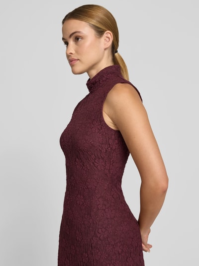 Frauenmodel trägt Maxikleid mit Allover-Spitzenbesatz von ROTATE im Elastischer-Material-Mix mit Baumwoll-Anteil, Slim-Fit, Stehkragen, ärmelloses Design, bordeauxrote Farbe, florale Struktur, Nahaufnahme Oberkörper von der Seite.