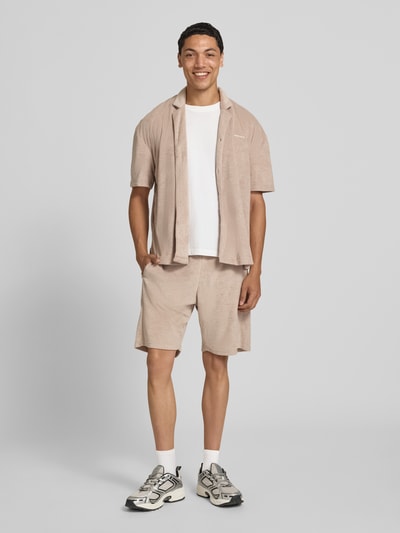 Männermodel trägt Relaxed Fit Freizeithemd mit Logo-Stitching Modell 'Nelas' von Pegador in Beige, Material-Mix mit Baumwoll-Anteil, Reverskragen, Knopfleiste, Ganzkörperansicht von vorne. Rückenlänge 71 cm, Schulterbreite 56 cm, Ärmellänge 24 cm.