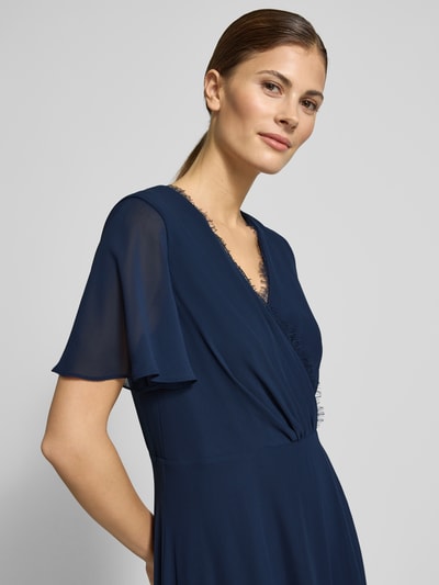 Frauenmodel trägt Damen Abendkleid mit Spitzenbesatz von Christian Berg Cocktail in Dunkelblau, taillierte Passform, V-Ausschnitt, Wickel-Optik, kurzärmelig, semitransparent, mit Raffungen, Nahaufnahme Oberkörper.