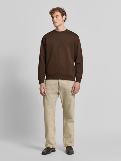 Mannenmodel draagt slim fit pullover van pure katoen 'TOM' van Selected in bruin, gecombineerd met lichte jeans, heren sweatshirt, volledig frontale lichaamsaanzicht.