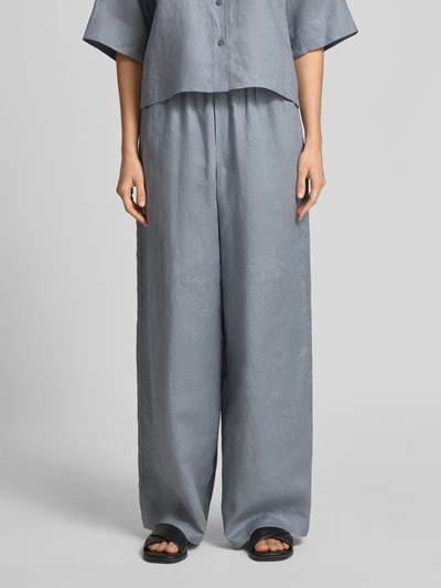 Modelka nosi szare, szerokie spodnie z lnu Wide Leg Leinenhose Modell 'DWINDLE' od Drykorn z elastycznym pasem, wiązane, struktura gładka, szerokość w rozmiarze 27/34: 38 cm, długość nogawki od wewnątrz: 83 cm, ujęcie frontalne do połowy ciała.