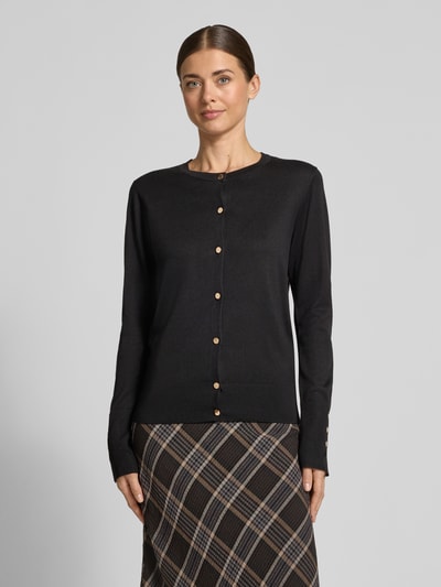 Modelka kobieca nosi Strickjacke aus Viskose-Mix mit Knopfleiste Modell 'Katie' od FREE/QUENT, czarny kolor, krój regular fit, prążkowane wykończenia, pełna długość rękawów, widoczna listwa guzikowa, widoczna faktura materiału, przód z przodu, długość tyłu w rozmiarze S: 59 cm, długość rękawa w rozmiarze S: 62 cm, zdjęcie całej sylwetki z przodu.