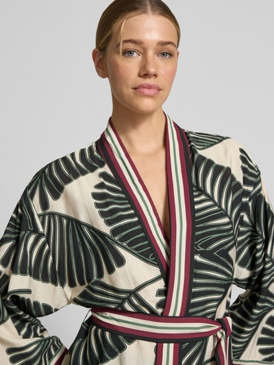 Frauenmodel trägt Kaftan aus Viskose-Mix mit floralem Allover-Print von Christian Berg Woman Selection, cremige Grundfarbe, grüne Blattmuster, schmale rot-grün-weiß gestreifte Ränder, abnehmbares Stoffband, taillierte Passform, Nahaufnahme Oberkörper.
